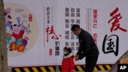 一名男子带着小女孩走过北京街头一面中国政府的宣传社会主义核心价值观的宣传墙。(2021年3月7日)