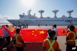 资料照:斯里兰卡港口工人在中国一带一路项目汉班托塔港手持中国国旗欢迎一艘中国考察船到港。(2022年8月16日)