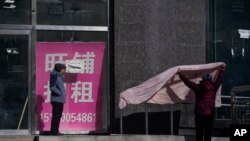 北京街头一名女子在一家空置招租店铺外晒被子。(2023年12月17日)
