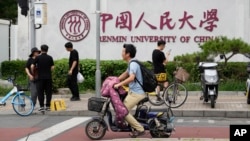 北京街头人们路过中国人民大学校园外墙的标识。(2024年7月22日)
