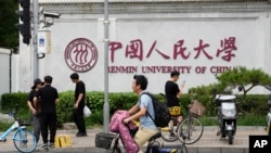 北京街头人们路过中国人民大学校园外墙的标识。(2024年7月22日)