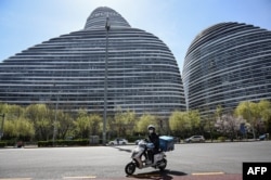 北京一名快递工人骑着电动车路过一处发现了新冠感染者的办公楼。(2022年4月7日)