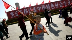 资料照:一个男孩手举红旗走过天安门广场上竖立的走中国特色社会主义道路的标语牌。(2007年10月9日)