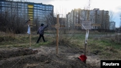 2022年4月4日,在乌克兰基辅地区的布查,一名男孩走过葬有平民尸体的坟墓。据当地居民称,这些平民是被俄罗斯士兵杀害的。(路透社)