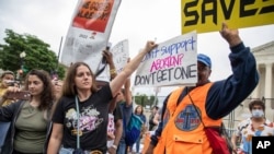 2022年5月14号,支持和反对妇女堕胎权利的美国民众聚集在美国最高法院外举行抗议活动。一名支持堕胎权利的女士试图用手里的标语牌遮盖她身旁一位反对堕胎的抗议人士手中的标语板。-照片来自美联社