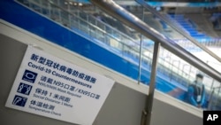 在北京一座室内体育馆的冰球场,一名工作人员站在写有如果防止感染新冠病毒措施的标牌附近。(资料照)