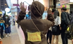 香港市民阿澧11月30日晚在旺角街站写心意卡给12港人,她在背上贴上标语,高举反送中运动”五大诉求、缺一不可”的手势。 (美国之音特约记者汤惠芸摄)