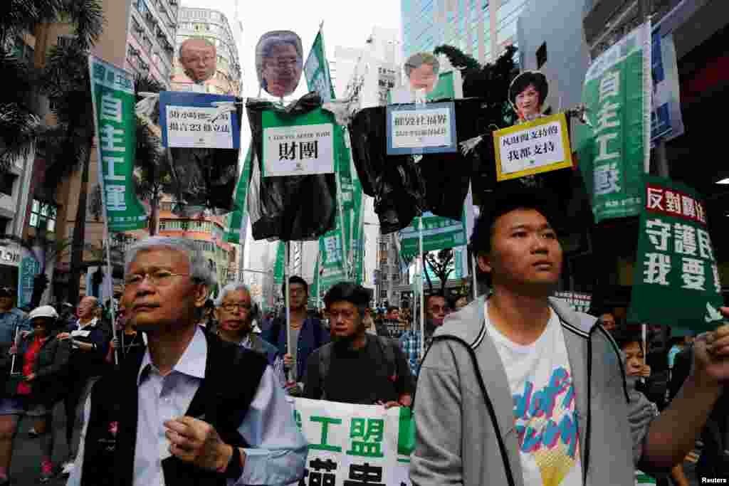 香港示威者举着标语牌:“反对释法,撤回复核,守护民选制度,我要真普选”,支持被香港政府司法复核,寻求撤销其立法会议员资格的刘小丽、姚松炎、梁国雄及罗冠聪。 还有人批判性地举着四位竞选特首者的头像,下面的标语强调这些候选人支持现有体制或者财团。 (2017年1月1日)