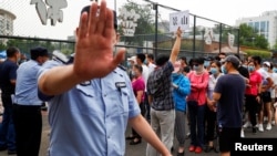 北京市民在一体育中心排队进行新冠病毒核酸检测,一名警察做出禁止的手式。(2020年6月17日)