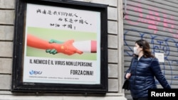 一名戴着口罩的妇女走过米兰街头一幅显示意大利与中国握手的广告牌。(2020年3月10日)