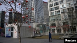 2020年2月18日星期二,只见一位戴口罩的女性在北京市中心商业区一座商业大楼前走过。