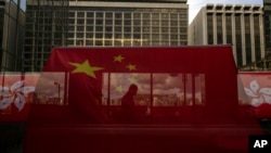 资料照:香港主权移交26周年纪念期间,中国国旗和香港区旗高挂香港街道大楼,旗帜后有行人走过天桥。(美联社,2023年6月27日)