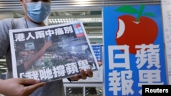 资料照:一名香港苹果日报员工在总部大楼的标识前手举最后一日发行的苹果日报。(2021年6月24日)
