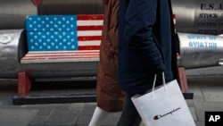 北京一对购物者提着从美国品牌Champion购买的商品,经过一条涂有美国国旗的长凳。(2019年2月13日)