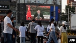 北京街头的行人观看电子屏幕上中国国家主席习近平通过视频在世卫大会视频开幕式上致辞。(2020年5月18日)
