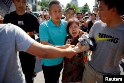 一名妇女在与一群记者谈论她目睹的美国驻北京大使馆外爆炸案后被警察抓住塞进一辆汽车。(2018年7月26日)