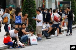资料照:中国游客在日本东京银座购物后坐在人行道路牙上休息。(2015年5月6日)