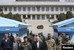 美国国务卿蒂勒森和美国上将、韩国上将在韩国和朝鲜之间的板门店停战村的南侧留影,北侧的朝鲜军人观看