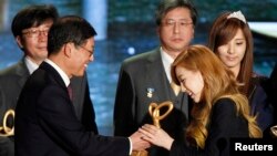 韩国流行歌曲女团“少女时代”的队长金泰妍(右二,Taeyeon)从韩国总理手里接过“总理表彰奖”。这个奖表扬“少女时代”对世界推广“韩流”的努力(2011年11月21日))