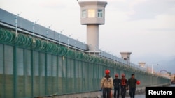 中国新疆维吾尔自治区达坂城的官方所谓的职业技能教育中心的围栏旁边,有工人走过。(2018年9月4日)