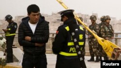 在中国新疆维吾尔自治区喀什的一条街上,警察检查一名男子的身份证,旁边有安全人员(2017年3月24日)