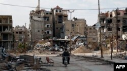 一名男子2月10日骑摩托车经过残破不堪的哈拉斯塔市(Harasta)。这座城市位于叙利亚首都大马士革以东。