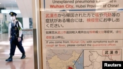 日本东京羽田机场一名戴着口罩的警察走过武汉肺炎的防疫广告牌。(2020年1月20日)