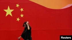 一名戴口罩的妇女经过一面画着中国国旗的墙。(资料照片)