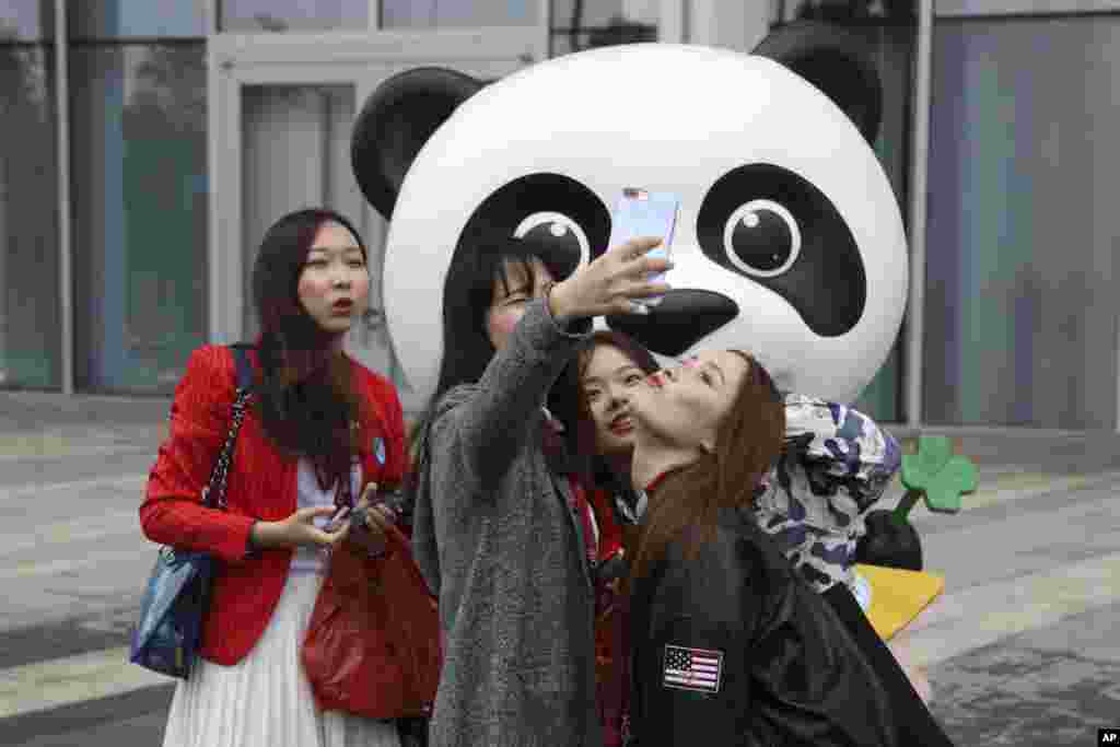 2018年11月5日,中国女孩在上海的中国国际进口博览会吉祥物熊猫前面摆姿势拍照,一位姑娘衣服上有美国星条旗的图案。